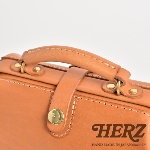 職人手作皮革口金醫生單肩包，展示了天然皮革材質的質感、精緻的手縫車線、黃銅色金屬扣環及圓形旋鈕，以及皮革提把。