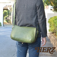 職人手作皮革復古翻蓋郵差包，採用綠色皮革製成，翻蓋設計，配有金色旋轉鎖扣和可調節的皮革肩帶，適合日常攜帶。