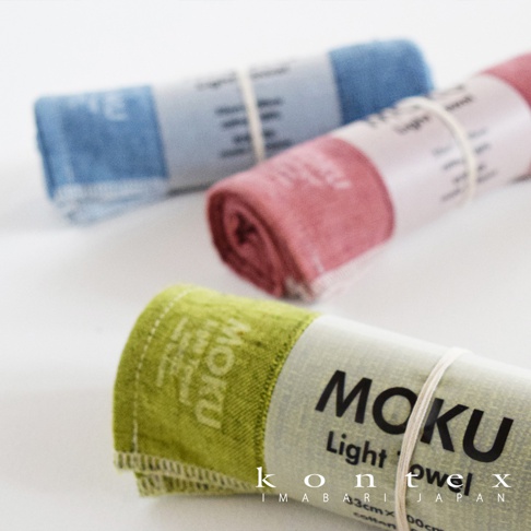 三條捲起的MOKU輕薄吸水長毛巾，顏色分別為藍色、粉紅色和綠色，皆以白色細繩綑綁，其中綠色毛巾的標籤清晰可見。