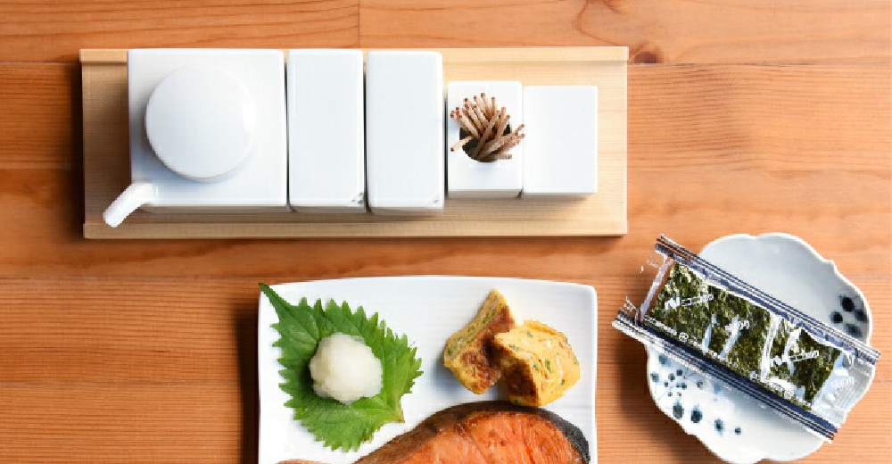 白色陶瓷調味五件組，含一個帶有傾斜壺嘴的醬油碟，以及裝有牙籤的方形容器，擺放在淺色木盤上。