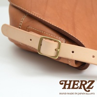 職人手作皮革郵差包，使用棕色皮革製成，配有淺色皮革的調節帶和金色方形扣環，展現精緻縫線細節。