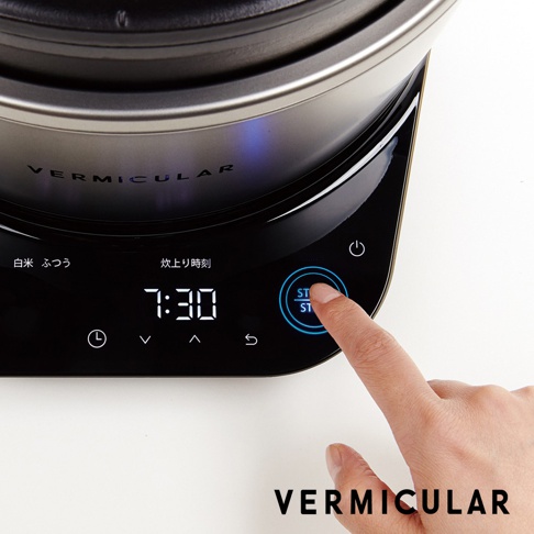 日本 Vermicular 琺瑯電子鑄鐵鍋，黑色觸控面板顯示「7:30」時間，一根手指正按下藍色光圈的「ST/ST」按鈕，鍋身印有「VERMICULAR」字樣。