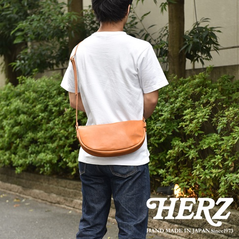 日本HERZ職人手作皮革半圓馬鞍包，由男性背著，展現茶色皮革的質感。