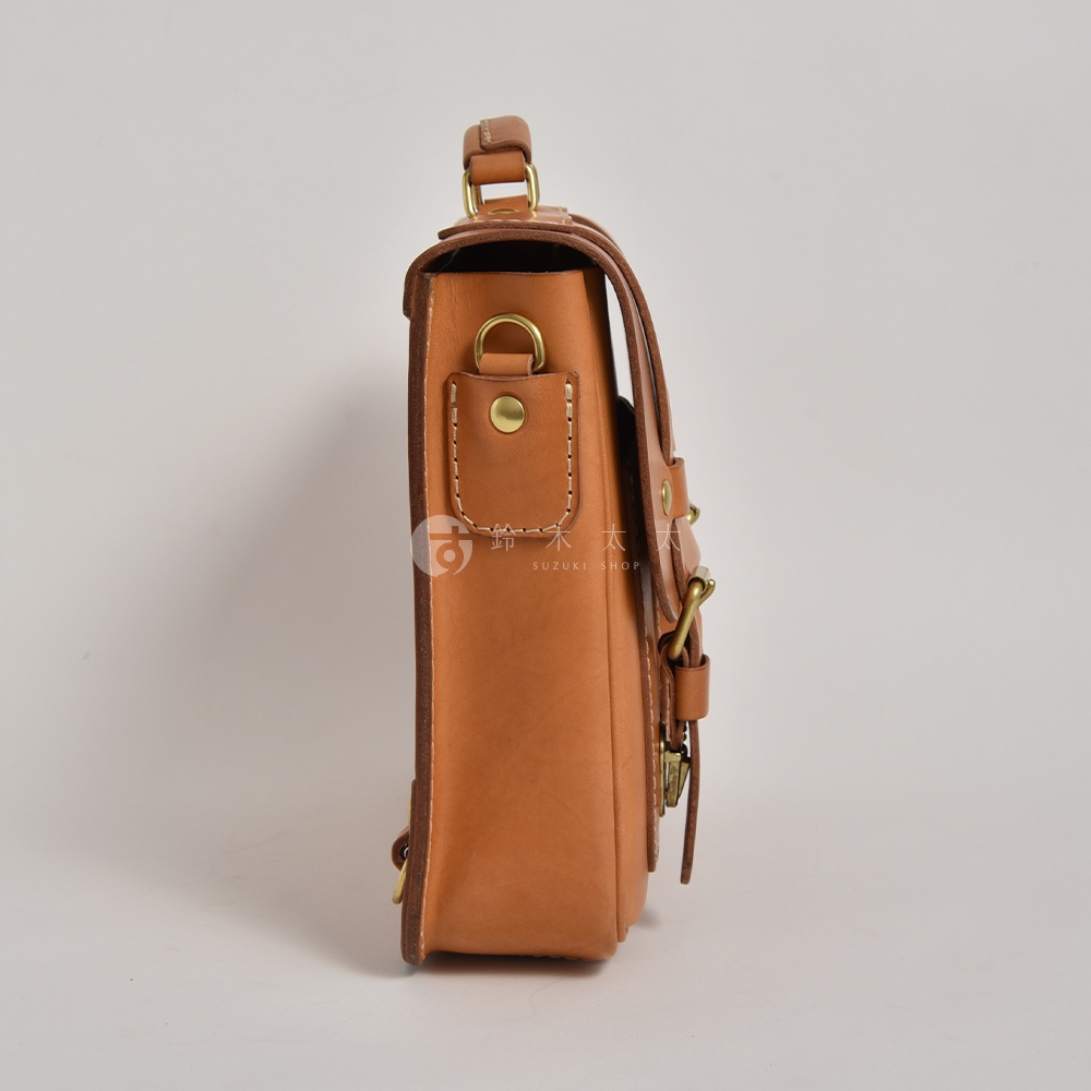 職人手作皮革傳統歐風三用學生包，側邊展示，淺棕色真皮材質，配有黃銅色金屬扣環及車縫線細節。