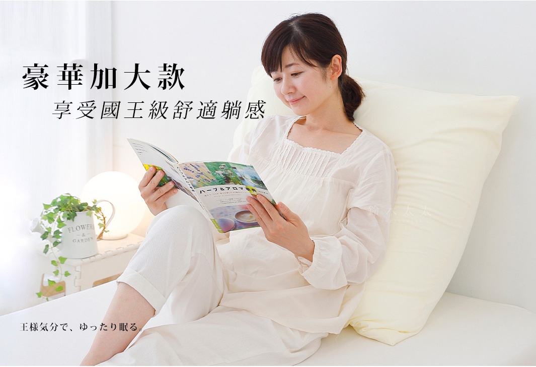 一位女子坐姿，身旁有一個大型淺黃色枕頭，女子穿著白色寬鬆長袖上衣和長褲，正在閱讀一本雜誌。