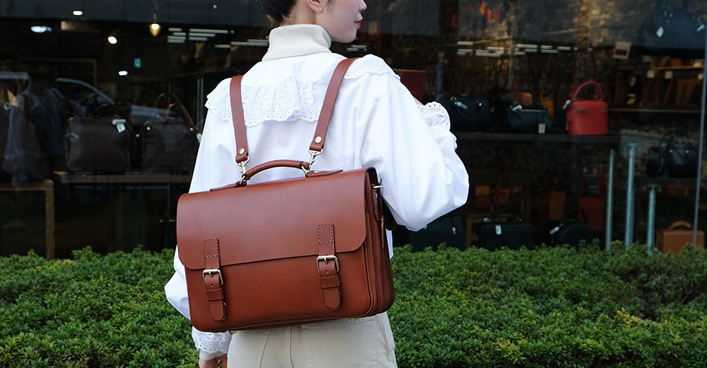 職人手作皮革極簡風三用商務公事包，採用棕色皮革製成，配有雙皮帶釦和金屬扣環，可手提、肩背或後背。