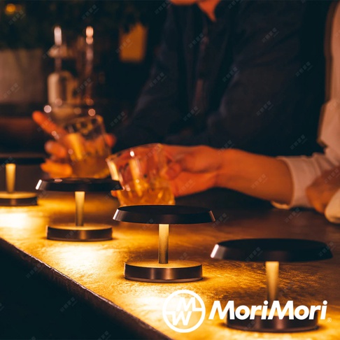 LED T-Light LOUNGE 工型造型燈，設有黑色圓形燈罩及金屬圓形底座，燈座中心為直立式金屬桿，散發溫暖黃光，營造氣氛。