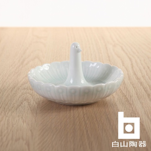 白色陶瓷製成，造型為站立的鳥，座為花瓣狀的淺碟，碟邊有浮雕裝飾。