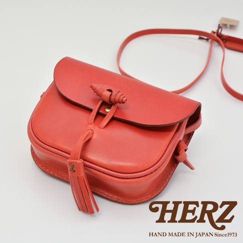 紅色皮革流蘇側背包，帶有圓弧形翻蓋和旋轉式鎖扣，皮革材質，精緻手工縫製。