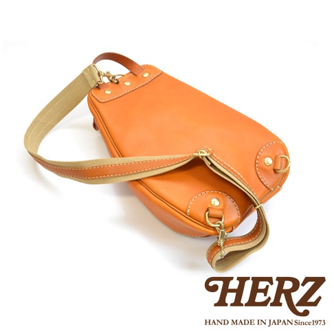 職人手作皮革多功能收納斜背包 F-3，橘棕色皮革，附有可調節的帆布與皮革製的斜背帶，以鉚釘及金屬扣環固定。