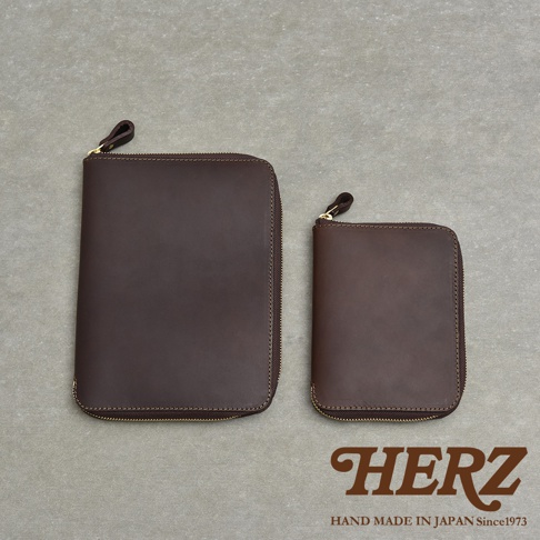 兩個深棕色皮革拉鍊記事本收納包，一大一小，放在灰色紋理背景上。