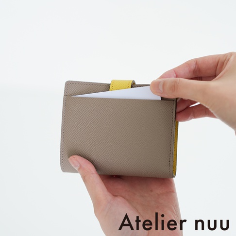 Atelier nuu 灰色皮革雙折短夾，黃色內襯，一隻手插入一張白卡。