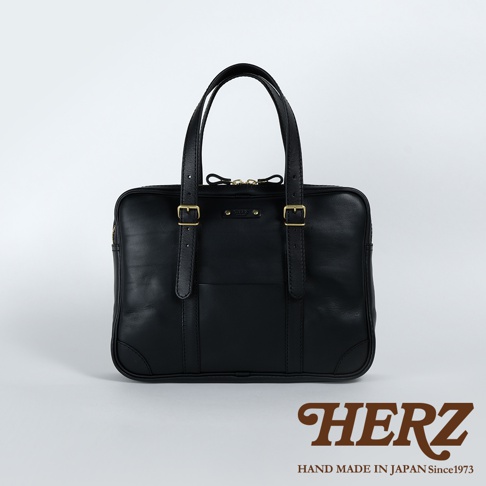 黑色皮革手提肩背兩用公事包，正面有雙提把、兩個金屬釦帶裝飾，以及一個開放式前袋。包包採用堅固的皮革材質，設計簡潔實用。