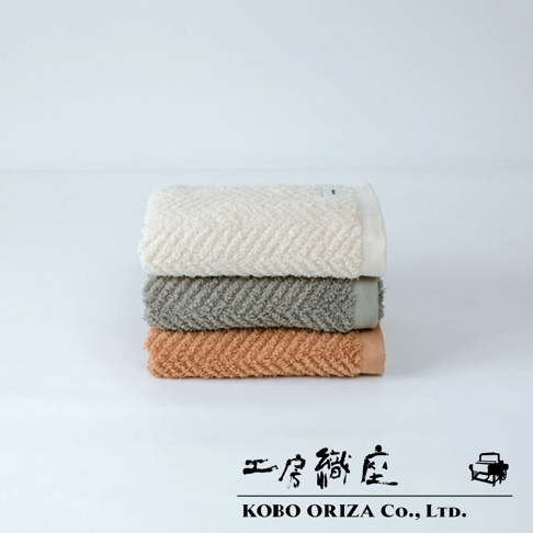 三條堆疊的 ECOR 天然系人字紋有機棉毛巾，顏色分別為米白、灰綠及橘棕。