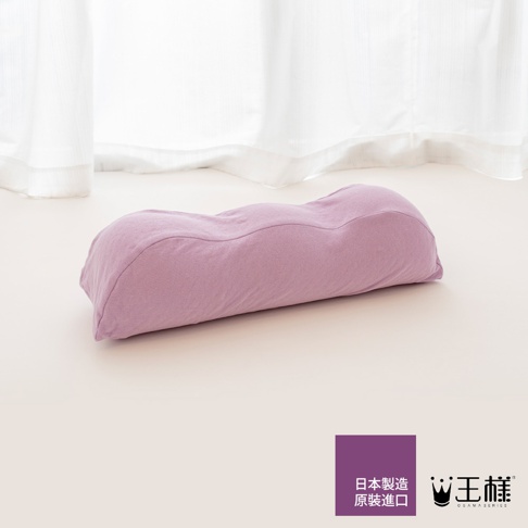 淡紫色波浪形抬腿枕，布料紋理清晰，枕身呈現人體工學曲線，置於淺色背景上，前方有日文標示「日本製造原裝進口」及品牌 Logo。