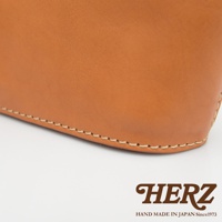 職人手作皮革三角收納包，淺棕色皮革，以米色線縫製邊緣，展現細膩工藝。