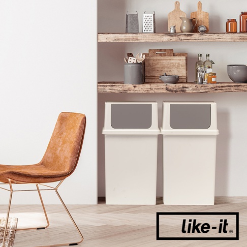 兩個白色塑膠前開式寬版可疊垃圾桶，垃圾桶蓋為深灰色，放置在木質地板上，背景有層架擺放廚房用品，左側有一張橘棕色皮革座椅。