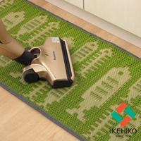 綠色藺草編織的長方形廚房地墊，織紋中帶有淺色圖案，邊緣為深灰色滾邊，一臺金屬色吸塵器頭正放在地墊上。