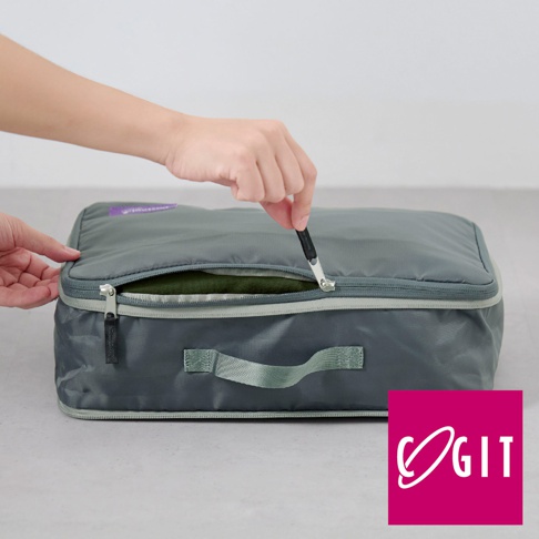 灰色折疊壓縮旅行袋，表面為防水尼龍材質，設有雙向拉鍊和提把，袋內可見綠色衣物。