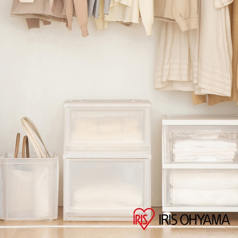 兩個透明的收納盒疊放在一起，左側有一個透明的方形收納籃，裡面放著衣架和木柄的工具。上方掛著淺色系的衣物。