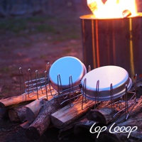 銀色不鏽鋼伸縮式瀝水架，架上擺放著兩個銀色金屬鍋蓋，背景是燃燒的營火。