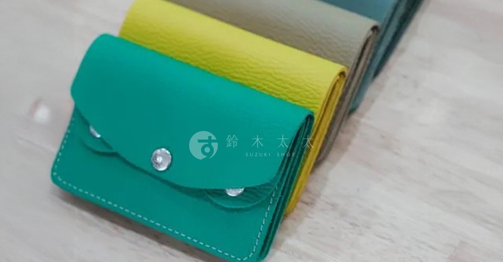 一排展示的京都職人手作隨身零錢包，從前景開始依序為：綠松石色、亮黃色、淺棕色、藍綠色。零錢包採用皮革材質，設計簡約，有銀色金屬按扣。