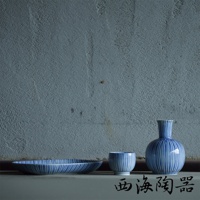 藍白條紋陶瓷點心碟、杯子及花瓶，器皿上飾有細緻的藍色十草紋，搭配粗糙的灰色水泥牆背景。