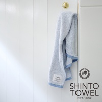 YUKINE 雪中漫步迷你浴巾，淺藍色，蓬厚柔軟的有機棉材質，帶有藍色滾邊，懸掛於白色木紋牆面。