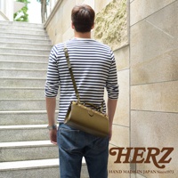 一位男士背著一個橄欖綠色的職人手作皮革復古口金兩用手提包，包包為圓筒狀，搭配長肩帶斜背，整體風格簡約。