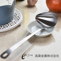 日製不鏽鋼橢圓尖嘴湯杓，湯勺呈銀色金屬光澤，置於白色陶瓷醬料碟中，湯勺柄上有掛孔，背景為淺色桌面，有洋蔥和蒜頭。