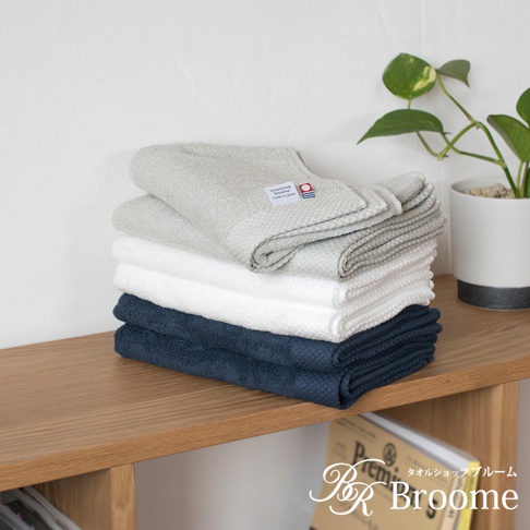 一疊今治純棉長毛巾，包含淺灰色、白色和海軍藍三種顏色。毛巾表面有菱形紋理，質感細膩，頂部淺灰色毛巾上帶有品牌標籤。