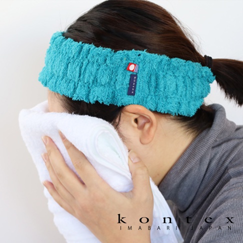 藍綠色毛巾材質髮帶，配有品牌標籤，一位女性正用白色毛巾擦拭臉部。
