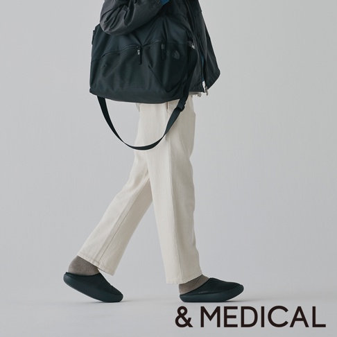 modello &MEDICAL KAMOLEG 3.0 美腳健身機能鞋，模特穿著奶油色褲子和灰色襪子，搭配黑色休閒鞋，肩上斜挎一個黑色大包。