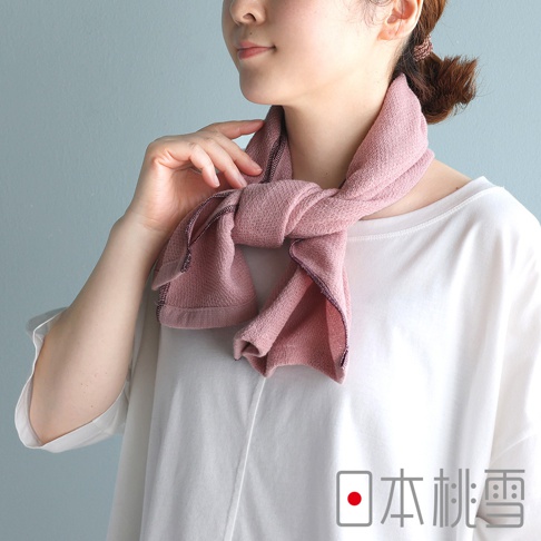 一位女性模特兒正佩戴著日本桃雪品牌的粉色今治輕量快乾運動長毛巾，毛巾以優雅的結扣方式圍繞在頸部，展現柔軟的質地與細緻的收邊細節，整體風格簡約舒適。