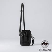 黑色皮革迷你側背收納包，表面有顆粒紋理，配有可調節的黑色尼龍斜背帶，包身正面有黑色織帶及登山扣裝飾。