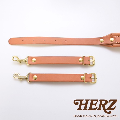 職人手作皮革加厚減壓肩背帶，展示了兩款不同長度的肩背帶。其中一款為淺棕色皮革，配有黃銅色鉤扣和固定鈕扣，另一款為淺棕色皮革，配有黃銅色調節扣和固定鈕扣。