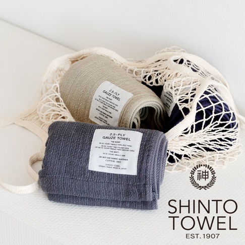 灰色、米白色和深藍色的2.5層紗浴巾，部分置於網狀收納袋中，展示其柔軟的材質與精緻的織紋。