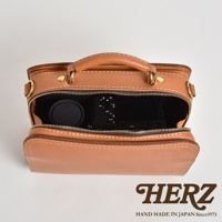 職人手作皮革兩用方形單肩包，淺棕色皮革，拉鍊開口，內有黑色相機及鏡頭蓋，包包有提把及金屬扣環，側邊與底部有縫線裝飾。