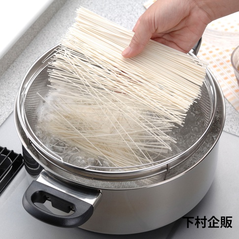 手持一束細長麵條，準備放入裝有滾水的不鏽鋼深型料理濾網籃中。濾網籃置於鍋內，網孔清晰可見。