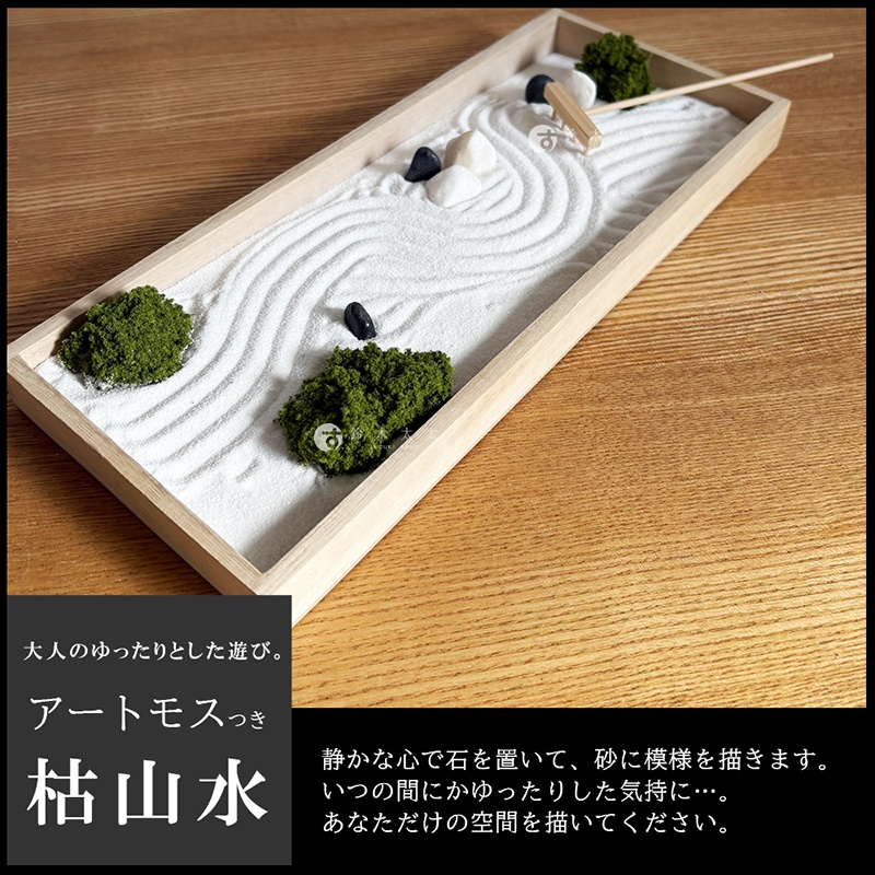長方形木製托盤內擺放著縮小版的枯山水庭園，細緻的白沙被耙子劃出層層波浪紋理，點綴著幾塊黑白相間的小石子與蓬鬆的綠色青苔裝飾，呈現出靜謐禪意與日式庭園的微縮景觀。
