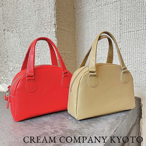兩款京都職人手作半月迷你手提包，一款為亮紅色，另一款為淺卡其色。兩款包皆為皮革材質，帶有圓潤的半月形包身和簡潔的提把設計，並配有拉鍊開合。