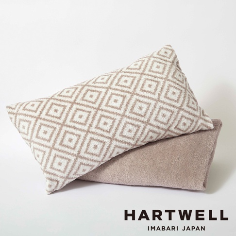 米白色菱形格紋枕套堆疊在淺褐色毛巾上， ambos 呈現柔軟的絨毛質感。