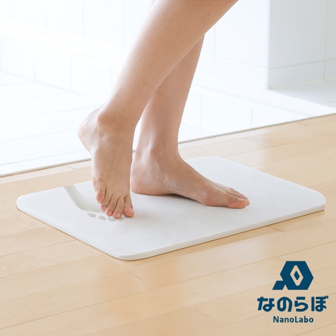 一雙裸腳踩在白色珪藻土瞬間吸水地墊上，地墊邊緣圓潤，表面有腳印。