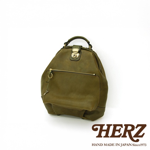 職人手作皮革輕旅行後背包 R-144，採用柔軟質感的皮革製成，呈現復古的墨綠色調。包款設有頂部提把、前方拉鍊口袋及翻蓋鎖扣，簡潔實用的設計適合日常或短途旅行。