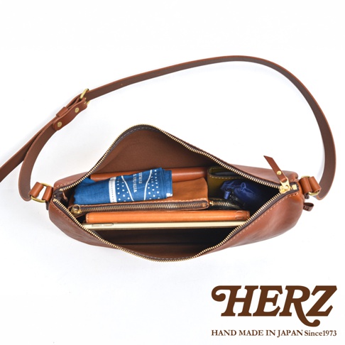 日本 HERZ 品牌皮革半圓馬鞍包，內部裝有藍色手帕、褐色皮夾和筆記型電腦，展示了包包的收納空間。
