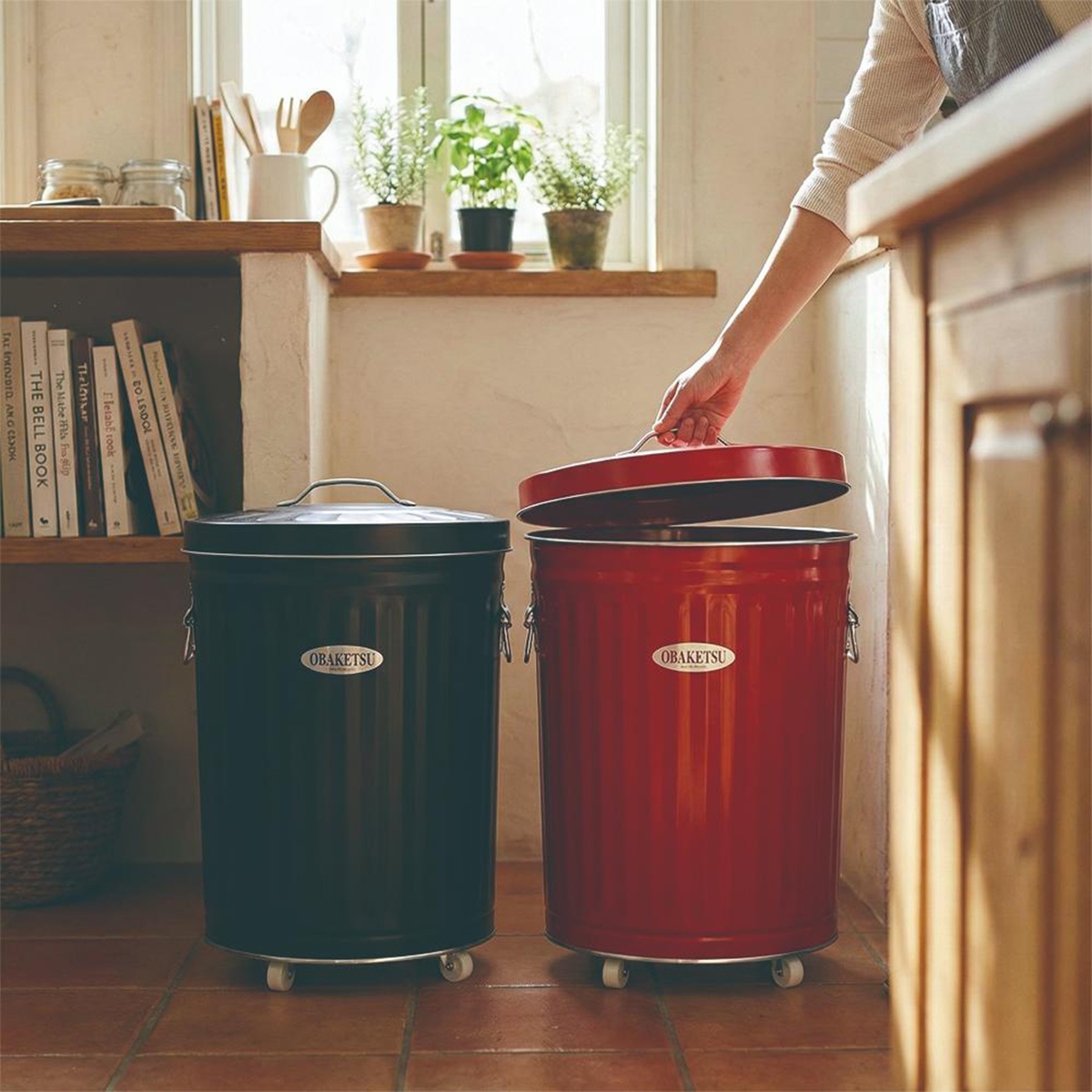 OBAKETSU 經典款附輪手工垃圾桶，一個黑色一個紅色，紅蓋垃圾桶的蓋子被提起
