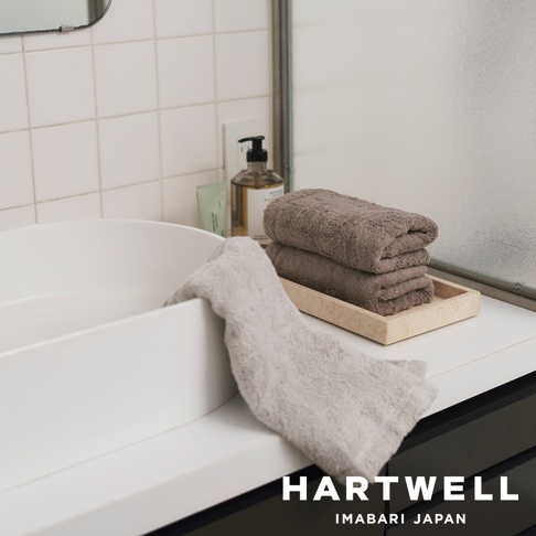 兩條柔軟的今治毛巾，一條為淺灰色，另一條疊放在淺棕色托盤上，呈現深棕色。