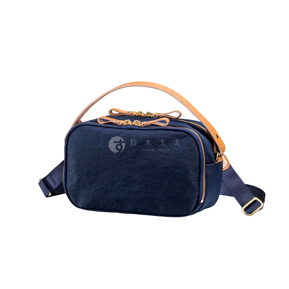 TUTUMU 經典防潑水兩用斜背包，採用深藍色尼龍材質，配以棕色皮革提把與斜背帶，質感金屬拉鍊與日本SUZUKI SHOP字樣標誌，展現簡約日系風格。