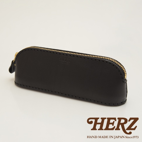 黑色皮革製成的職人手作三角弧形收納筆袋，配有金色拉鍊和品牌壓紋，縫線精緻。