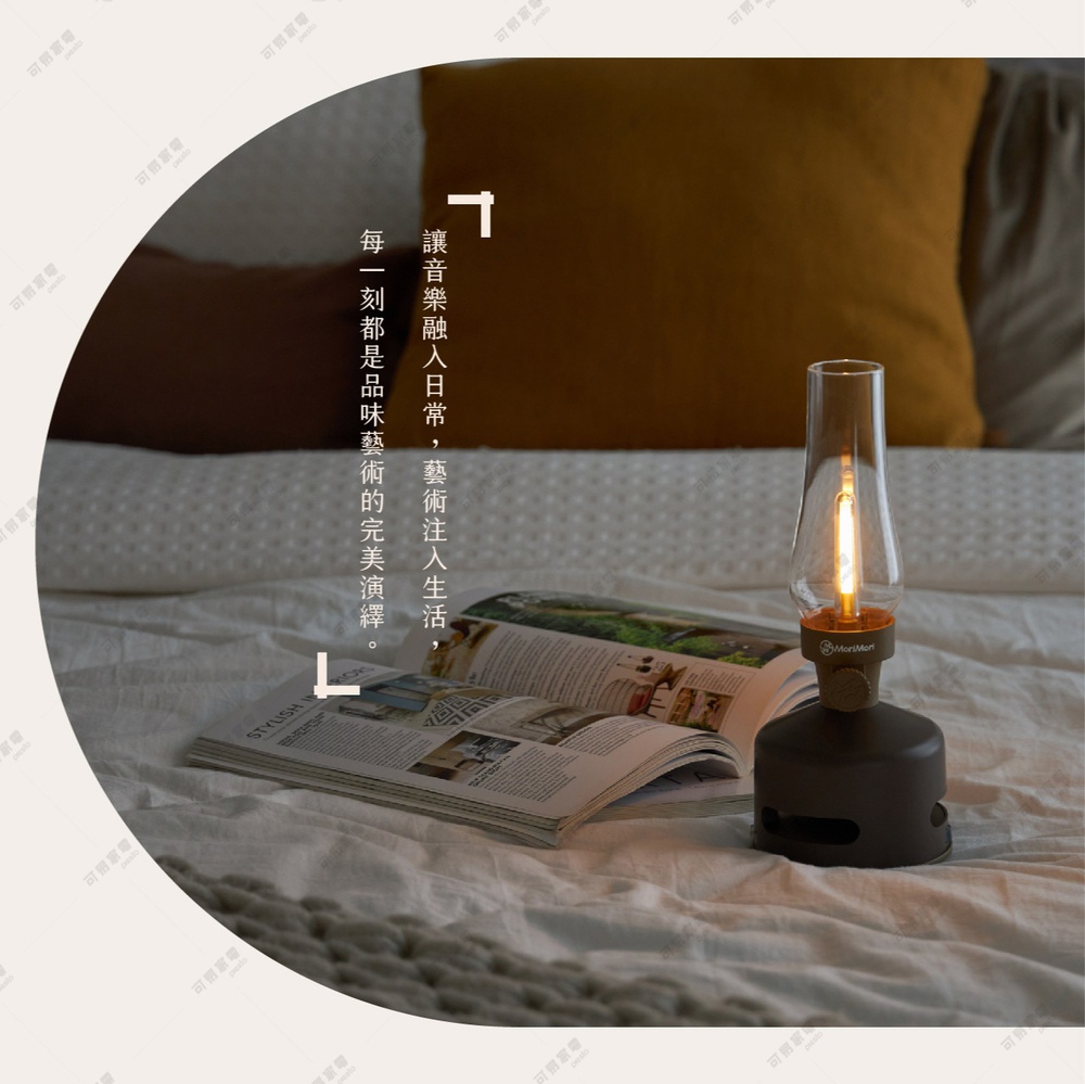 煤油燈造型藍牙音響，深棕色底座，透明玻璃燈罩內有LED燈芯，置於床鋪上，旁邊放著一本翻開的雜誌。